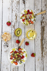 Erdbeer-Kiwi-Joghurt mit Müsli, Chiasamen, Agavensirup in Glasschale auf Holz - SARF001915