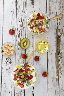 Erdbeer-Kiwi-Joghurt mit Müsli, Chiasamen, Agavensirup in Glasschale auf Holz - SARF001915