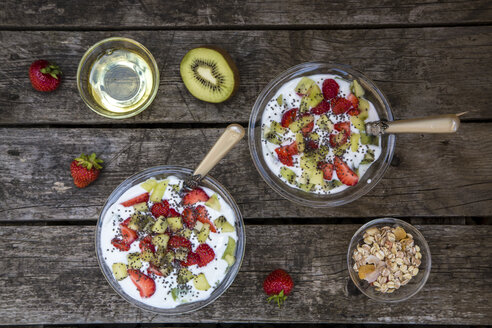 Erdbeer-Kiwi-Joghurt mit Müsli, Chiasamen, Agavensirup in Glasschale auf Holz - SARF001916