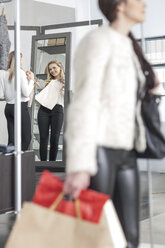 Woman holding top looking in mirror in a boutique - ZEF006693