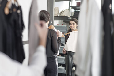 Woman holding top looking in mirror in a boutique - ZEF006694