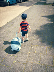 Toddler child pulling his luggage while walking away down the road. Goettingen, Germany. - ABAF001817