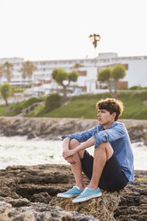 Griechenland, Rhodos, junger Mann sitzt am Meer und schaut in die Ferne - WDF003144