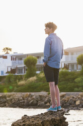 Greece, Rhodes, young man standing on a rock at seafront looking at distance - WDF003145