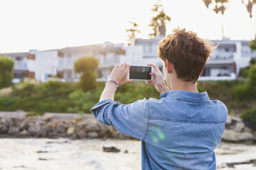 Griechenland, Rhodos, junger Mann fotografiert mit Smartphone an der Strandpromenade - WDF003149