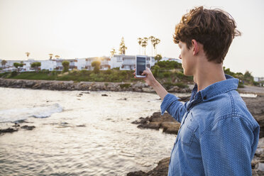 Griechenland, Rhodos, junger Mann fotografiert mit Smartphone an der Strandpromenade - WDF003150