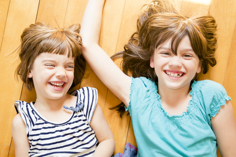 Portrait of two laughing sisters lying on wooden floor stock photo