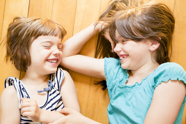 Two laughing sisters lying on wooden floor - LVF003517