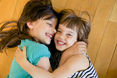 Two happy sisters hugging on wooden floor - LVF003518