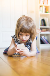 Little girl lying on wooden floor with smartphone - LVF003533