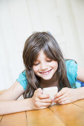 Lächelndes Mädchen auf Holzboden liegend mit Smartphone - LVF003535