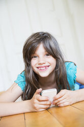 Porträt eines lächelnden Mädchens, das mit einem Smartphone auf dem Holzboden liegt - LVF003530