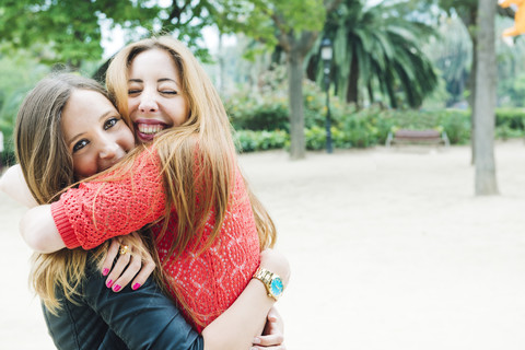 Zwei glückliche junge Frauen umarmen sich in einem Park, lizenzfreies Stockfoto