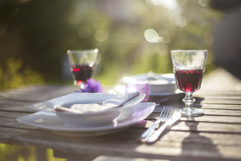 Gedeckter Gartentisch mit zwei Gläsern Rotwein bei Gegenlicht - SARF001923