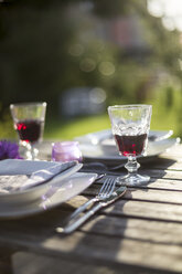 Gedeckter Gartentisch mit zwei Gläsern Rotwein bei Gegenlicht - SARF001924