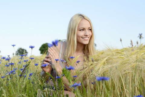 Lächelnde junge Frau hockt auf einem Feld, lizenzfreies Stockfoto