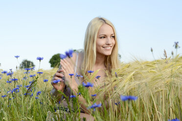 Lächelnde junge Frau hockt auf einem Feld - BFRF001253
