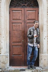 Italien, San Gimignano, junger Mann vor der Eingangstür, der sein Smartphone benutzt - GIOF000028