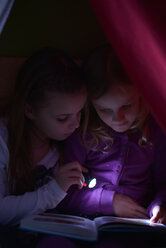 Zwei Mädchen lesen ein Buch mit einer Taschenlampe in ihrer selbstgebauten Höhle - NYF000003