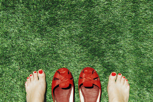 Barfüßige Frauen mit rot lackierten Nägeln neben einem Paar roter Schuhe, auf dem grünen Gras - GEMF000247