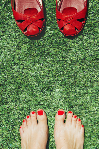 Barfüßige Frauen mit rot lackierten Nägeln neben einem Paar roter Schuhe, auf dem grünen Gras, lizenzfreies Stockfoto