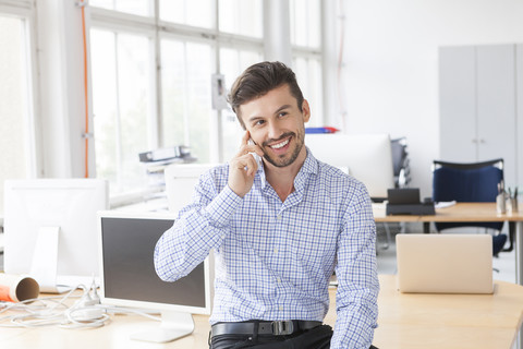Porträt eines lächelnden Geschäftsmannes beim Telefonieren in einem Büro, lizenzfreies Stockfoto