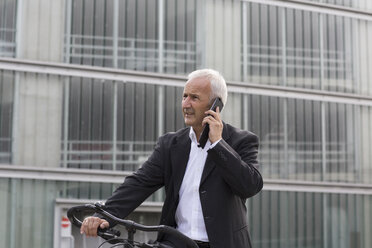 Businessman with bicycle telephoning with smartphone - SGF001708