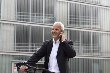Businessman with bicycle telephoning with smartphone - SGF001709