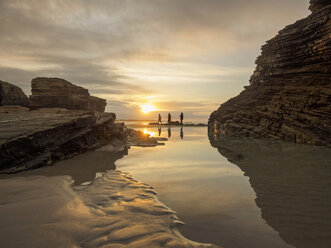 Spanien, Galicien, Ribadeo, Playa de Aguas Weihnachtsmänner bei Sonnenuntergang, kleine Personen am Strand - LAF001409