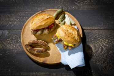 Nürnberger Rostbratwurst, Weizenbrötchen mit Senfketchup und Gewürzgurke auf Holzteller - MAEF010766