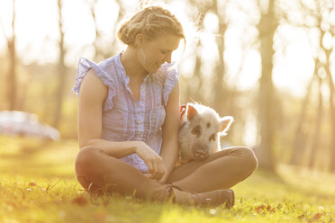 Smiling woman sitting with piglet in park - TAM000196