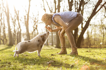 Woman taming piglet in park - TAM000197