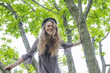 Porträt einer lächelnden jungen Frau, die auf einen Baum klettert - SGF001719