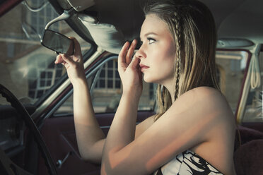 Young woman checking her make up in rear-view mirror of vintage car - TAM000203