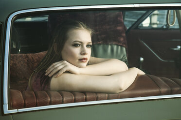 Portrait of young woman looking through rear window of vintage car - TAM000204