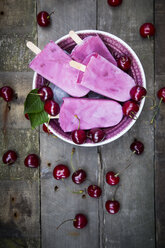 Bowl of cherry yoghurt ice lollies and cherries on wood - LVF003563