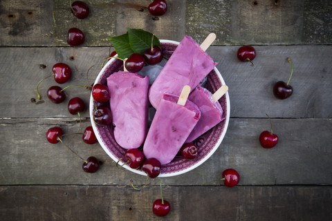 Schale mit Kirsch-Joghurt-Eislutschern und Kirschen auf Holz, lizenzfreies Stockfoto