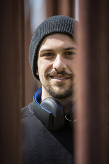 Porträt eines lächelnden jungen Mannes mit Kopfhörern und Wollmütze - TAM000208