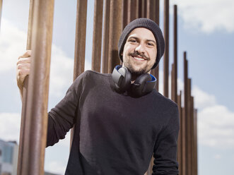 Portrait of smiling young man with headphones wearing wool cap and black pullover - TAM000209