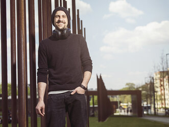 Portrait of smiling young man with headphones wearing wool cap and black pullover - TAM000210