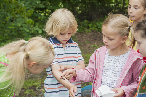 Deutschland, Kinder beobachten die Raupe eines Pfirsichfalters auf dem Arm eines Jungen - MJF001571