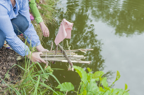 Deutschland, Frau setzt Spielzeugfloß ins Wasser - MJF001567