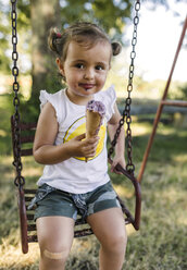 Porträt eines glücklichen kleinen Mädchens, das auf einer Schaukel sitzt und Eis isst - MGOF000306