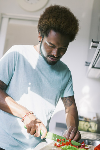 Junger Mann schneidet Gemüse in seiner Küche, lizenzfreies Stockfoto