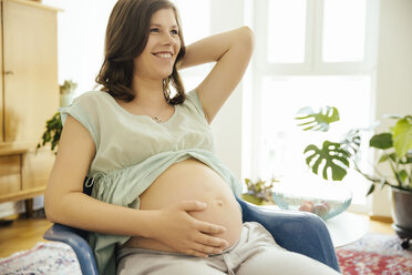 Glückliche schwangere Frau, die zu Hause auf einem Stuhl sitzt - MFF001759
