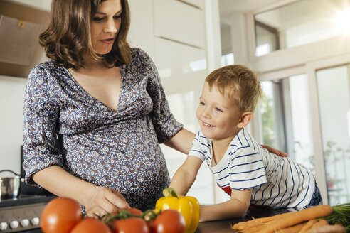 Schwangere Frau mit ihrem kleinen Sohn in der Küche bei der Zubereitung von Gemüse - MFF001763