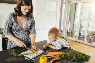 Pregnant woman cutting vegetables with her son in the kitchen - MFF001764