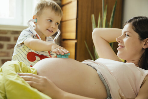 Kleiner Junge benutzt ein Spielzeugstethoskop, um den Bauch seiner schwangeren Mutter zu untersuchen - MFF001771