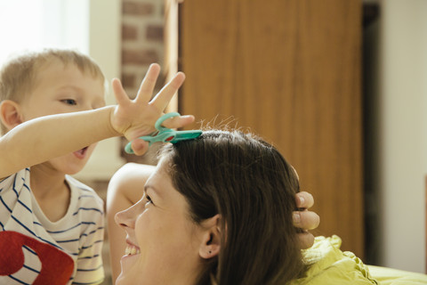 Kleiner Junge tut so, als würde er der Mutter zu Hause die Haare schneiden, lizenzfreies Stockfoto