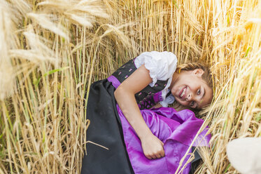 Deutschland, Sachsen, Porträt eines lächelnden Mädchens im Dirndl, das in einem Getreidefeld liegt - MJF001580